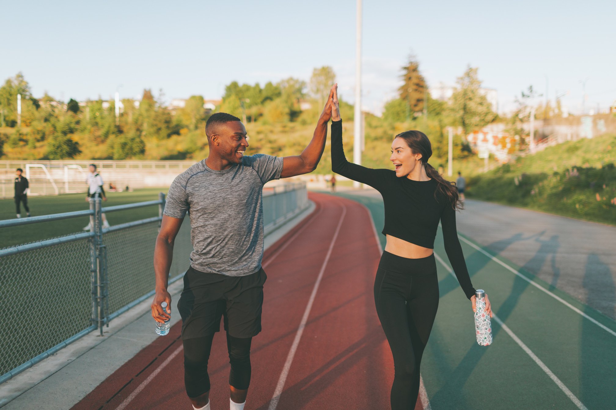 Happy Athletic Couple with Drinking Bottles Doing High Five Outdoors